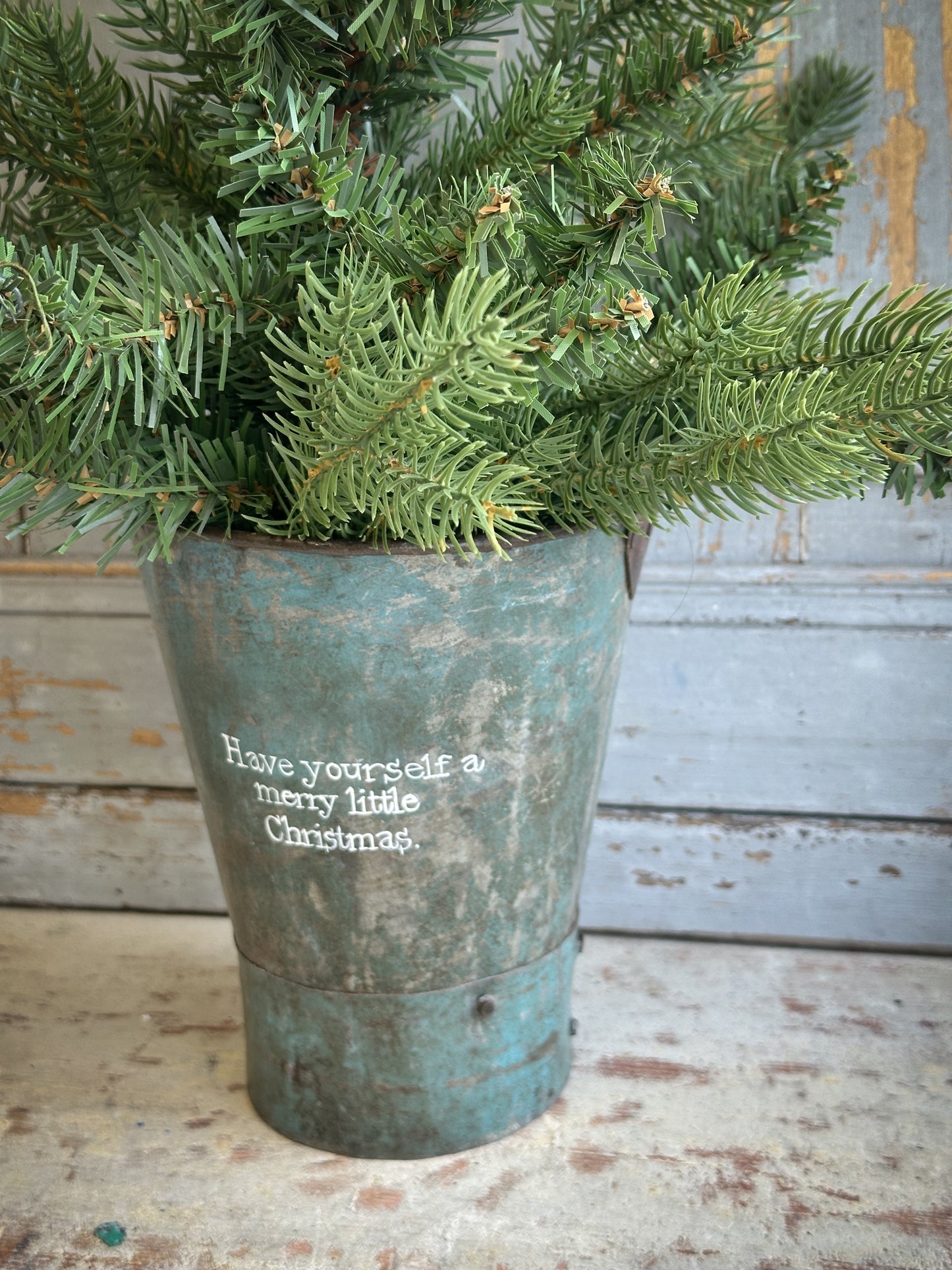 A Recycled Metal Mini Christmas Tree Bucket With A Hand Painted Quote