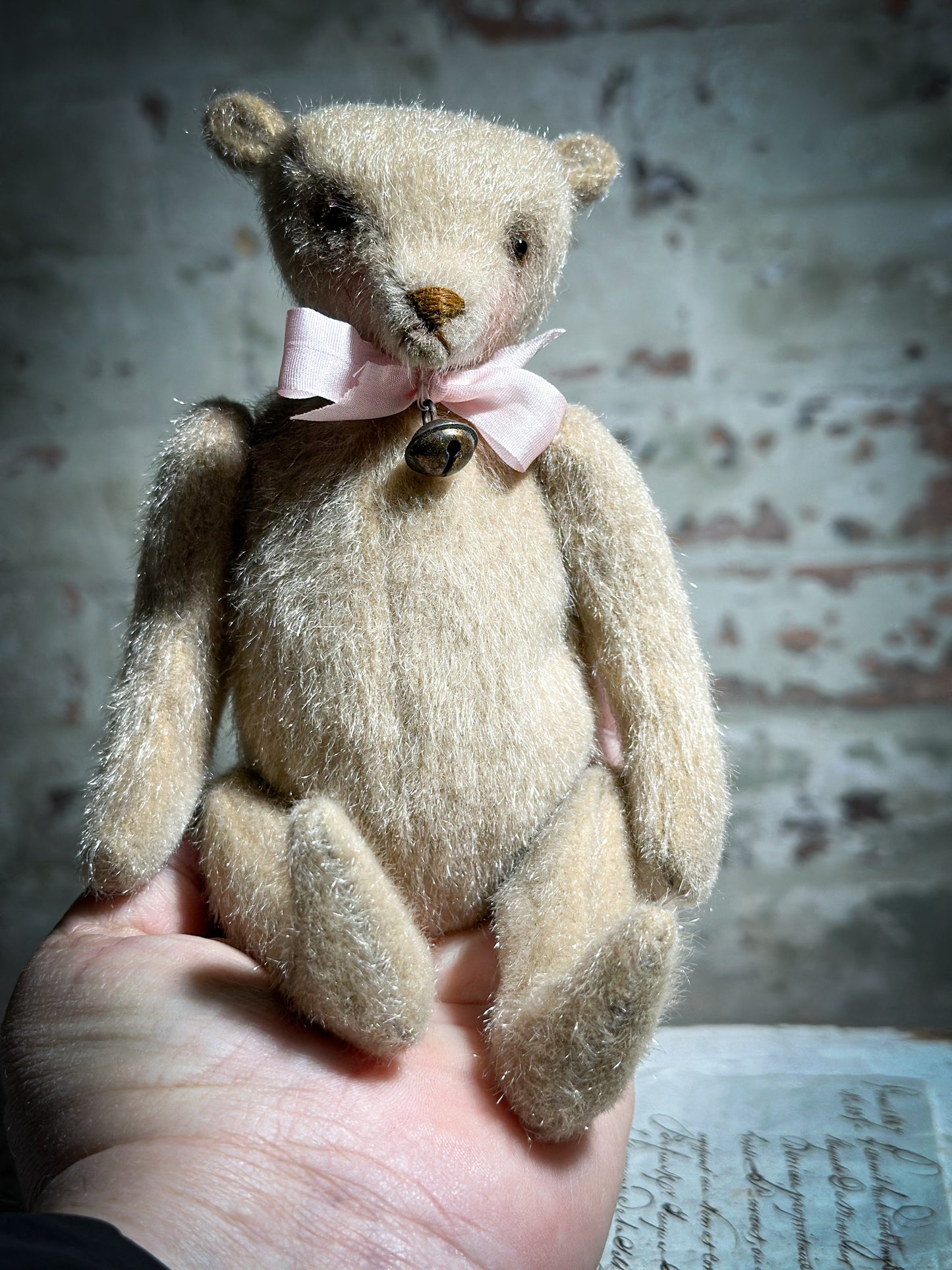 A beautiful hand made tiny jointed collector’s teddy bear with pale pink antique ribbon and bell and heart charm