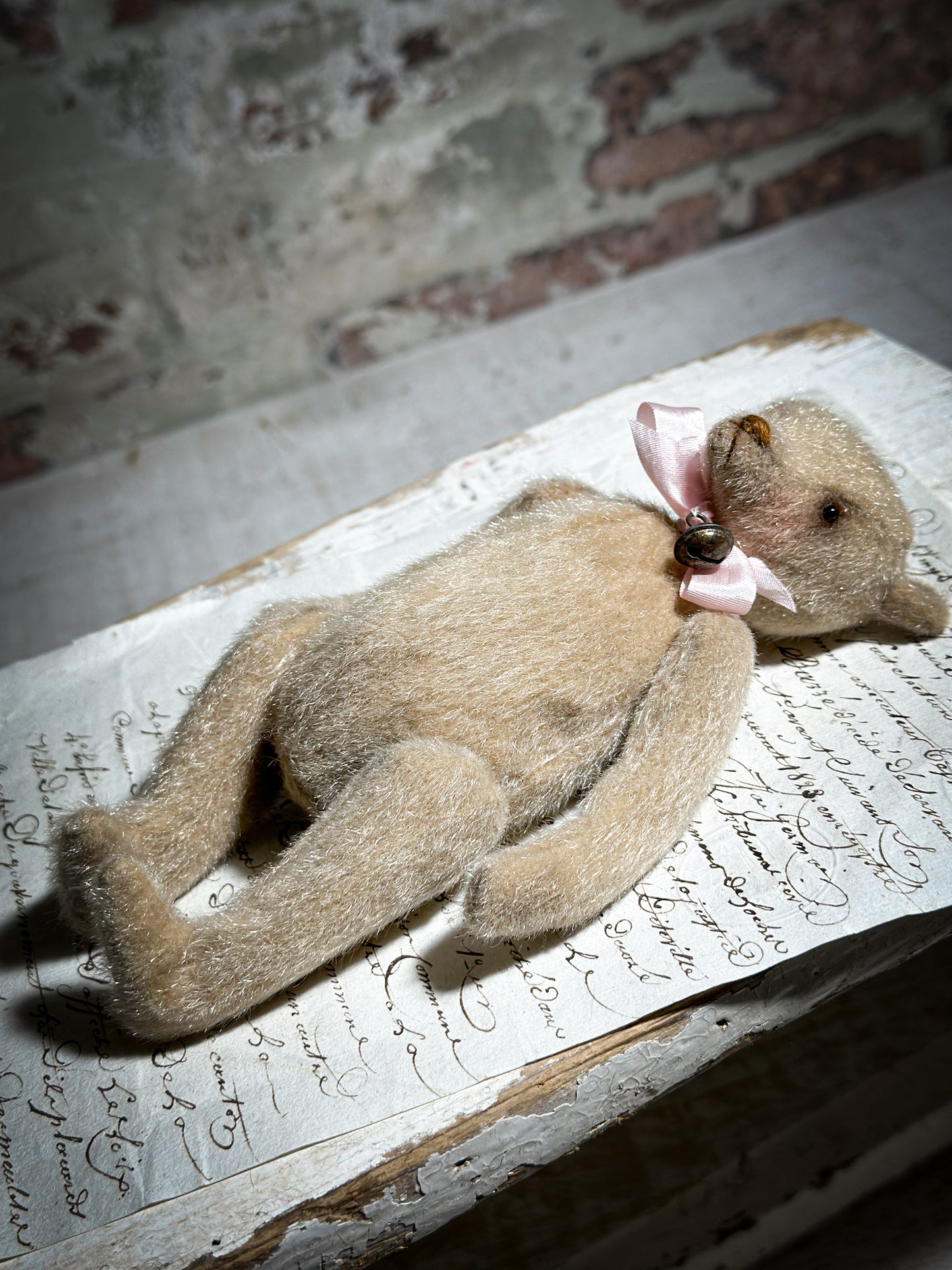 A beautiful hand made tiny jointed collector’s teddy bear with pale pink antique ribbon and bell and heart charm