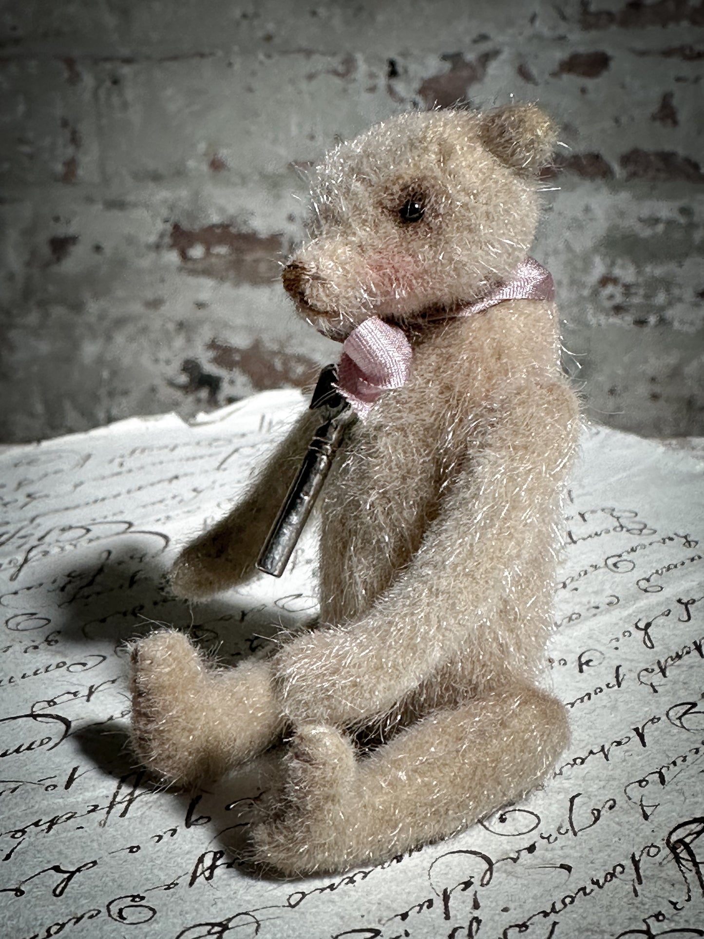 A beautiful hand made tiny jointed collector’s teddy bear with pale pink antique ribbon and bell and heart charm