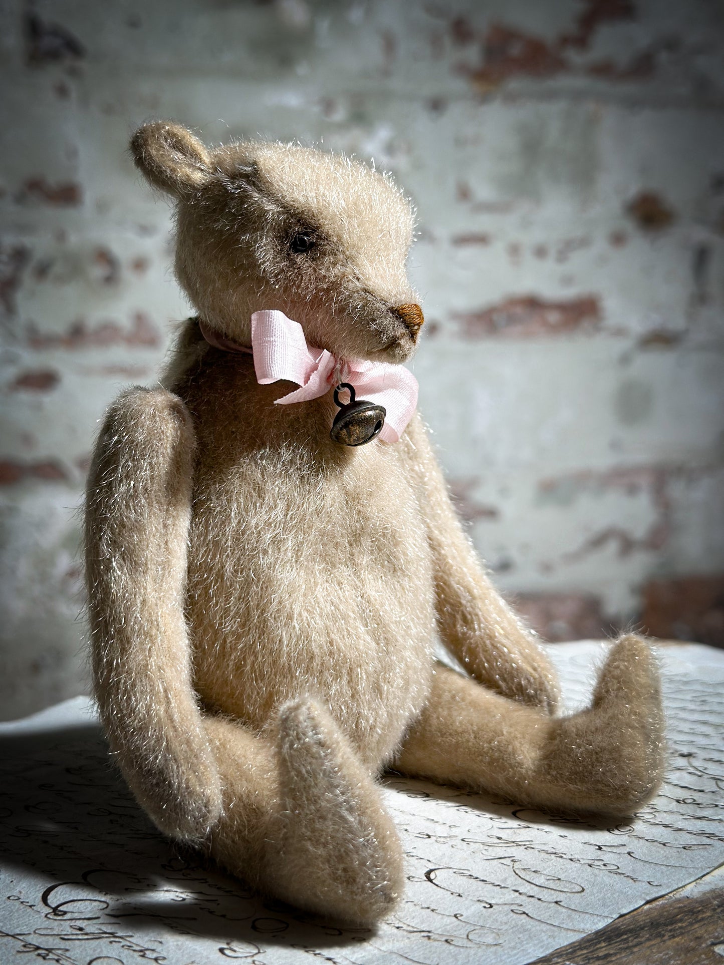 A beautiful hand made tiny jointed collector’s teddy bear with pale pink antique ribbon and bell and heart charm