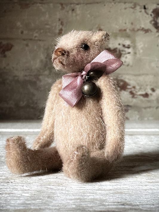 A beautiful hand made tiny jointed collector’s teddy bear with pale pink antique ribbon and bell and heart charm