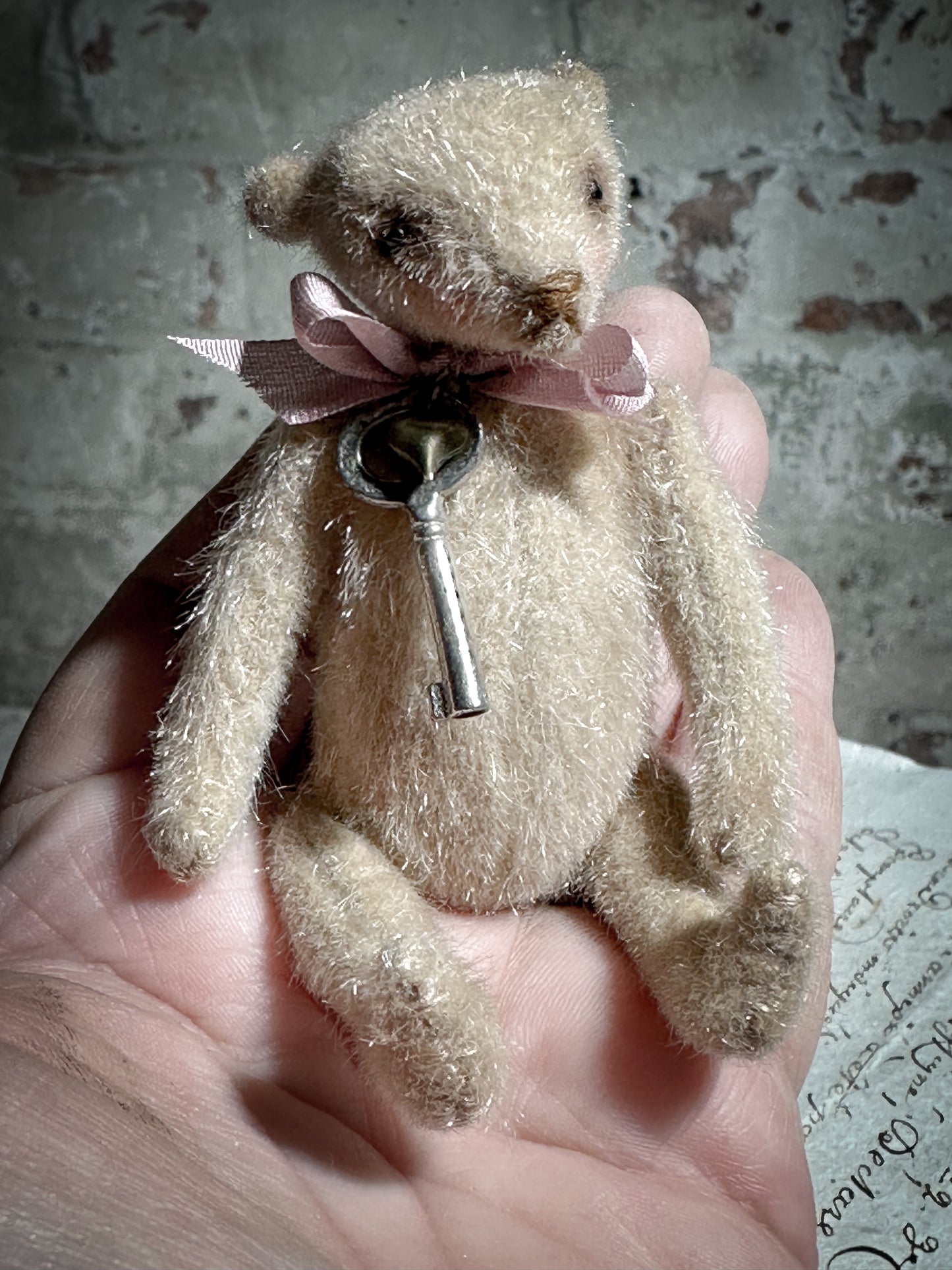 A beautiful hand made tiny jointed collector’s teddy bear with pale pink antique ribbon and bell and heart charm