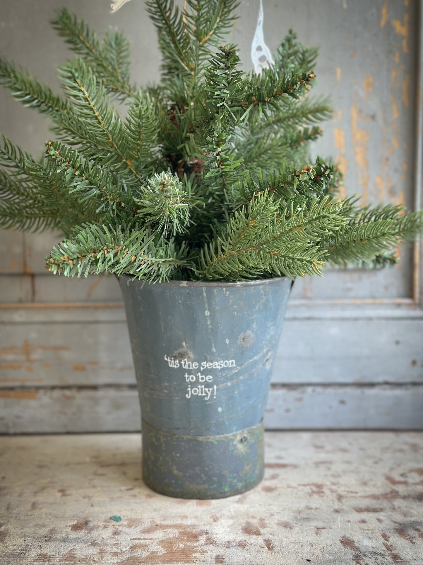 A Recycled Metal Mini Christmas Tree Bucket With A Hand Painted Quote