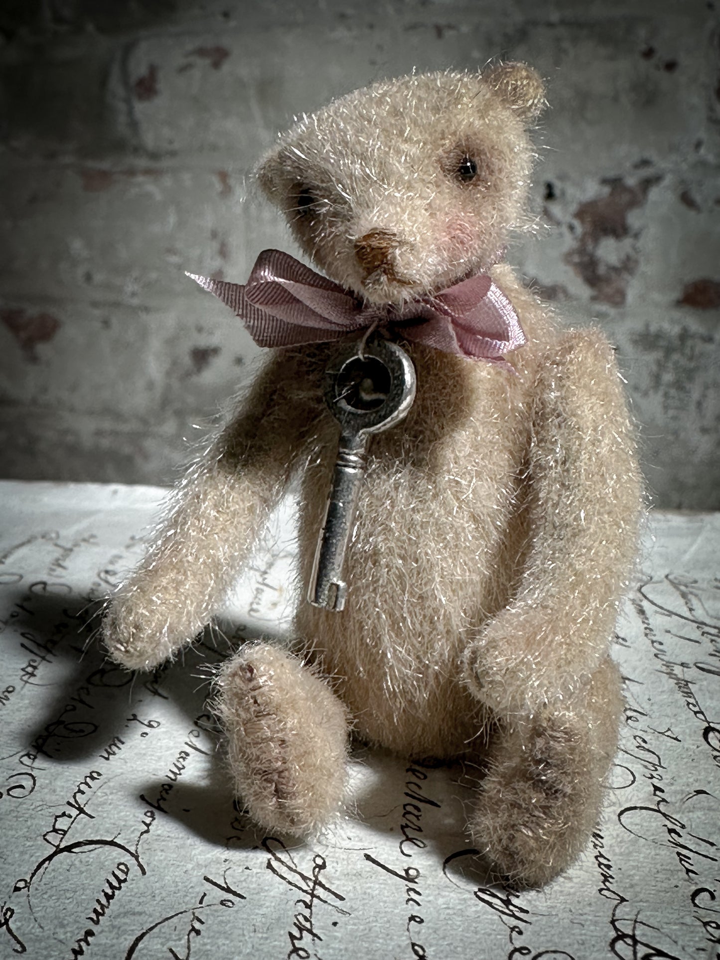 A beautiful hand made tiny jointed collector’s teddy bear with pale pink antique ribbon and bell and heart charm