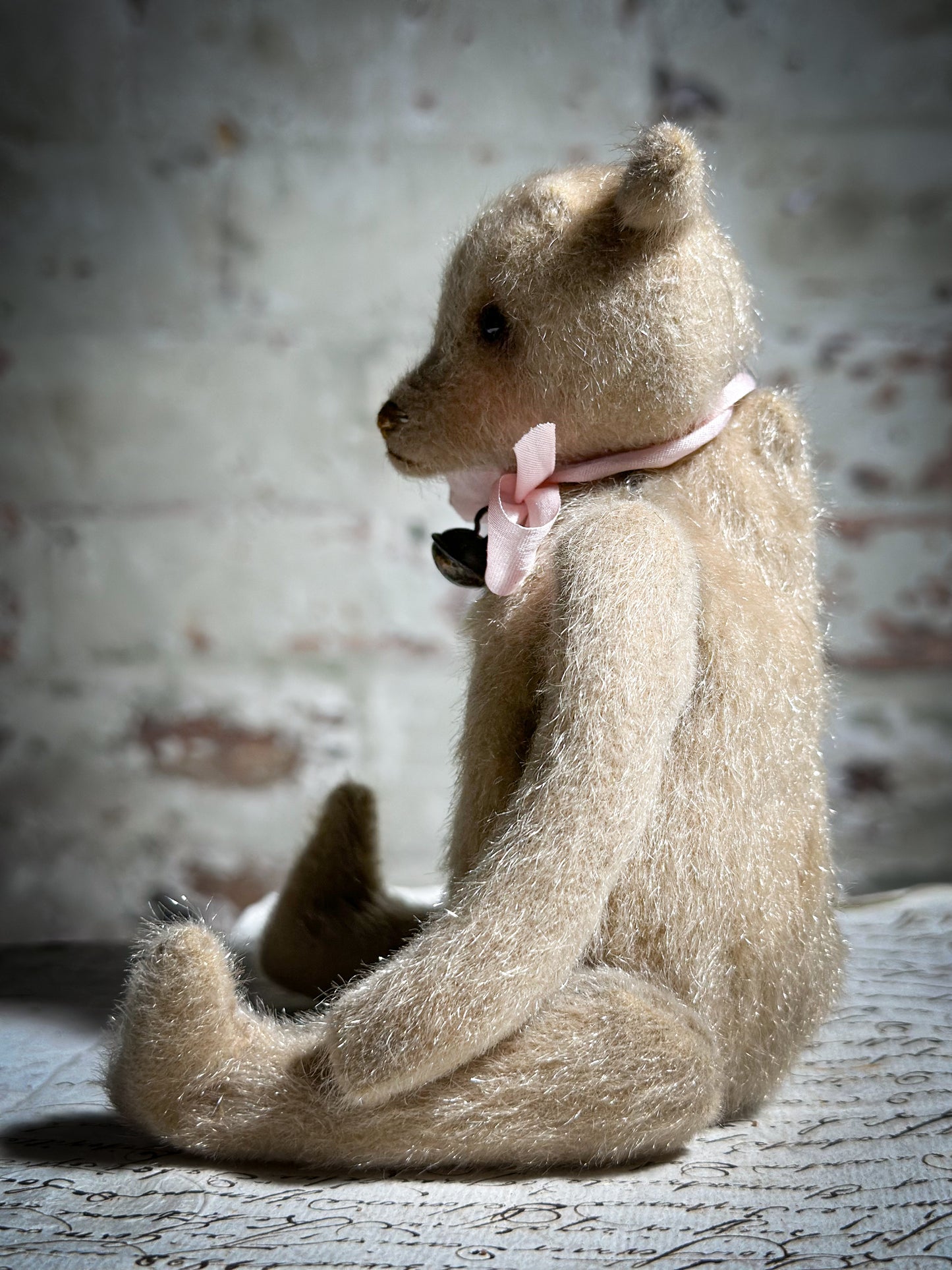 A beautiful hand made tiny jointed collector’s teddy bear with pale pink antique ribbon and bell and heart charm