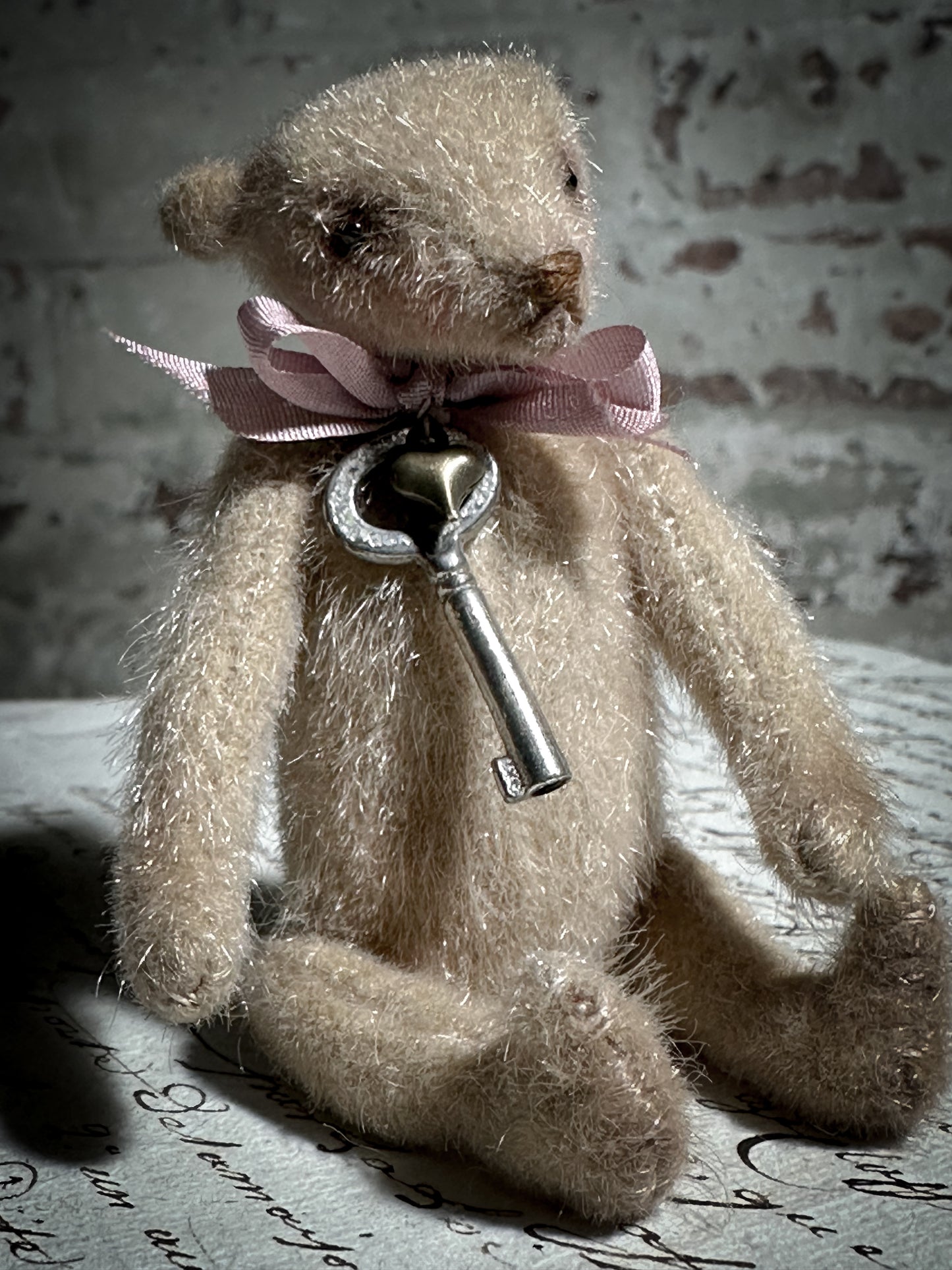 A beautiful hand made tiny jointed collector’s teddy bear with pale pink antique ribbon and bell and heart charm