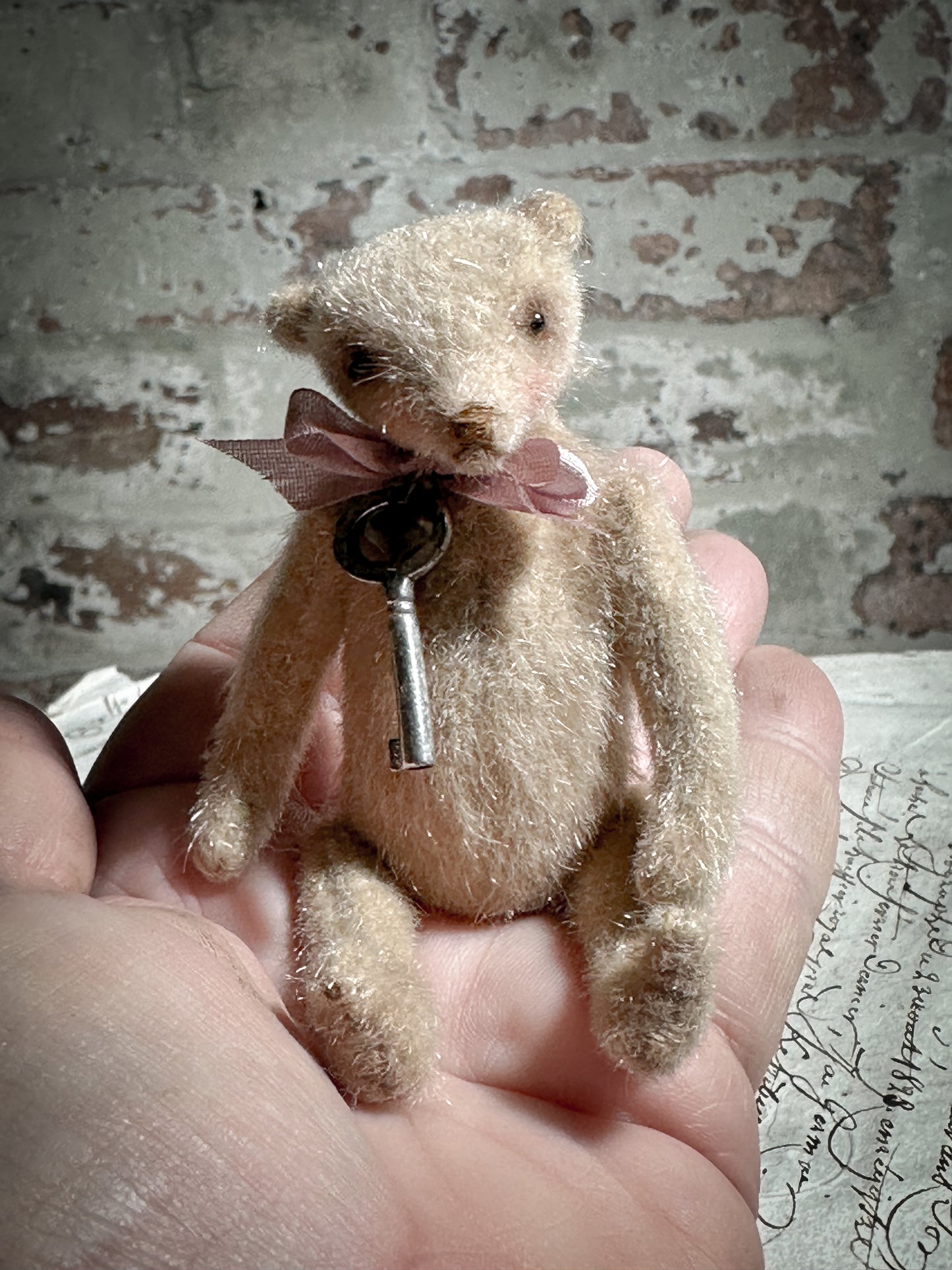 A beautiful hand made tiny jointed collector’s teddy bear with pale pink antique ribbon and bell and heart charm