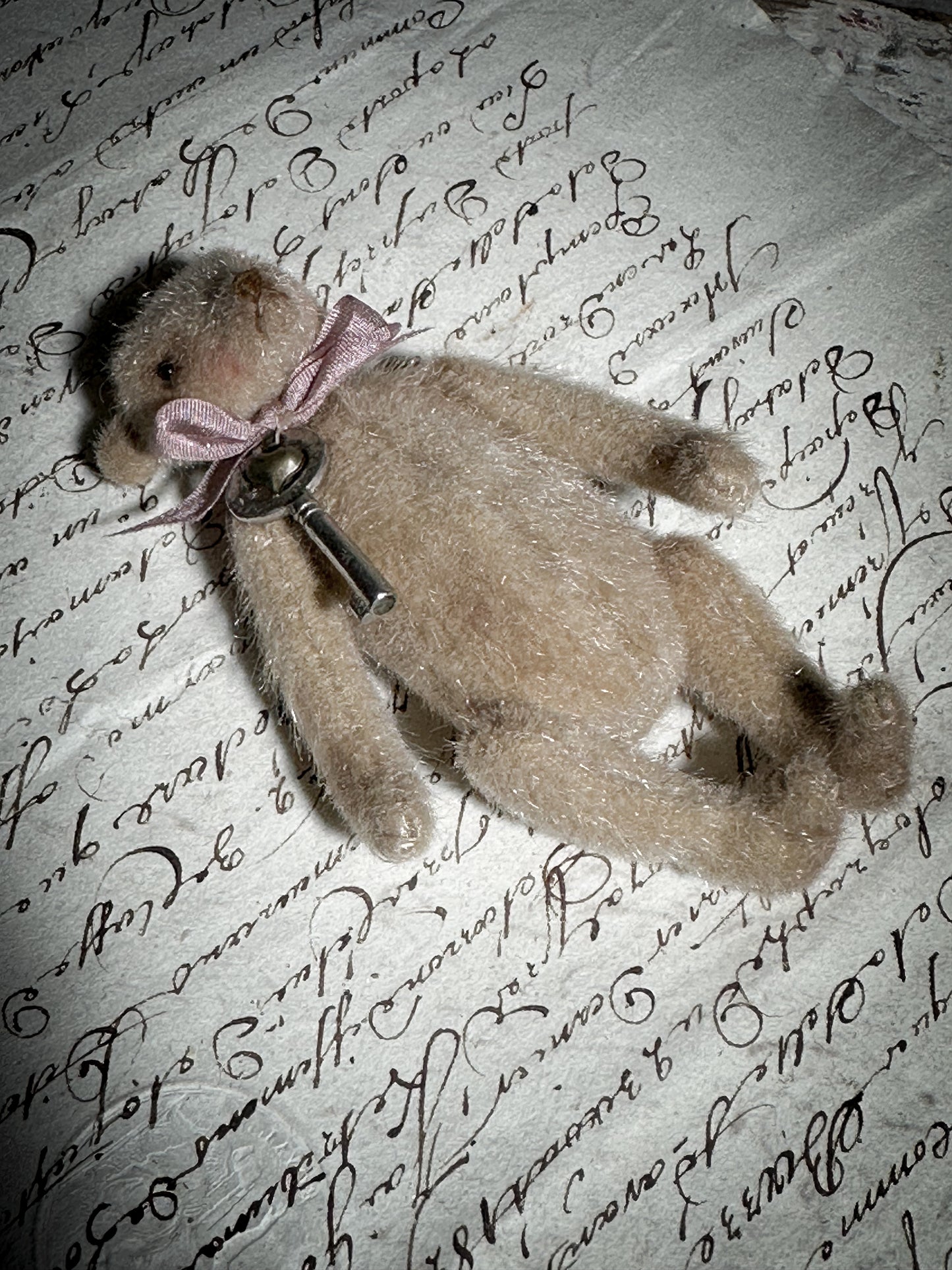 A beautiful hand made tiny jointed collector’s teddy bear with pale pink antique ribbon and bell and heart charm