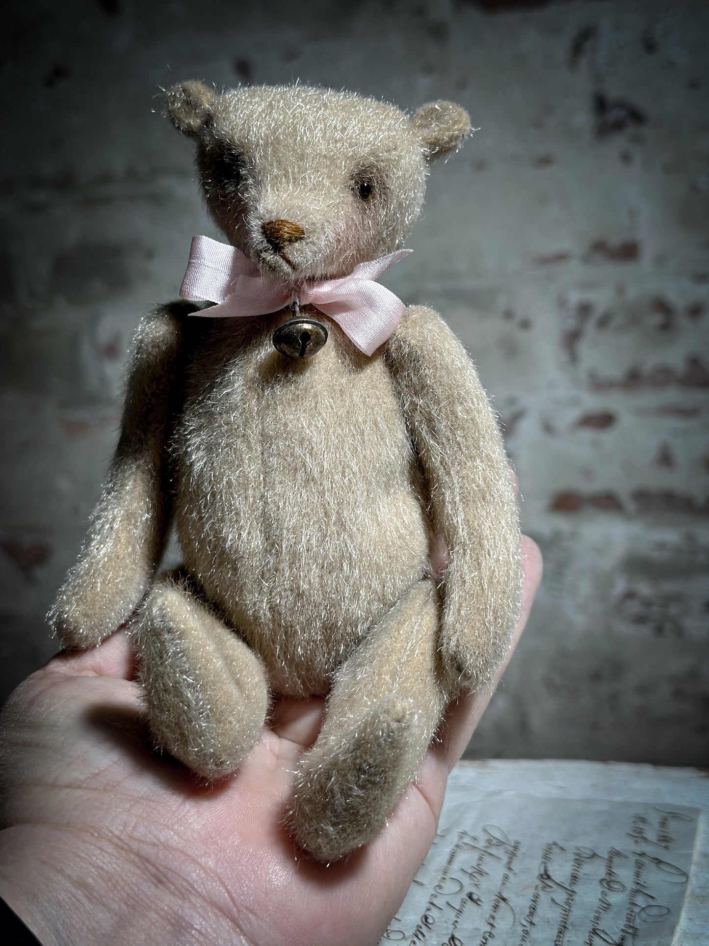 A beautiful hand made tiny jointed collector’s teddy bear with pale pink antique ribbon and bell and heart charm