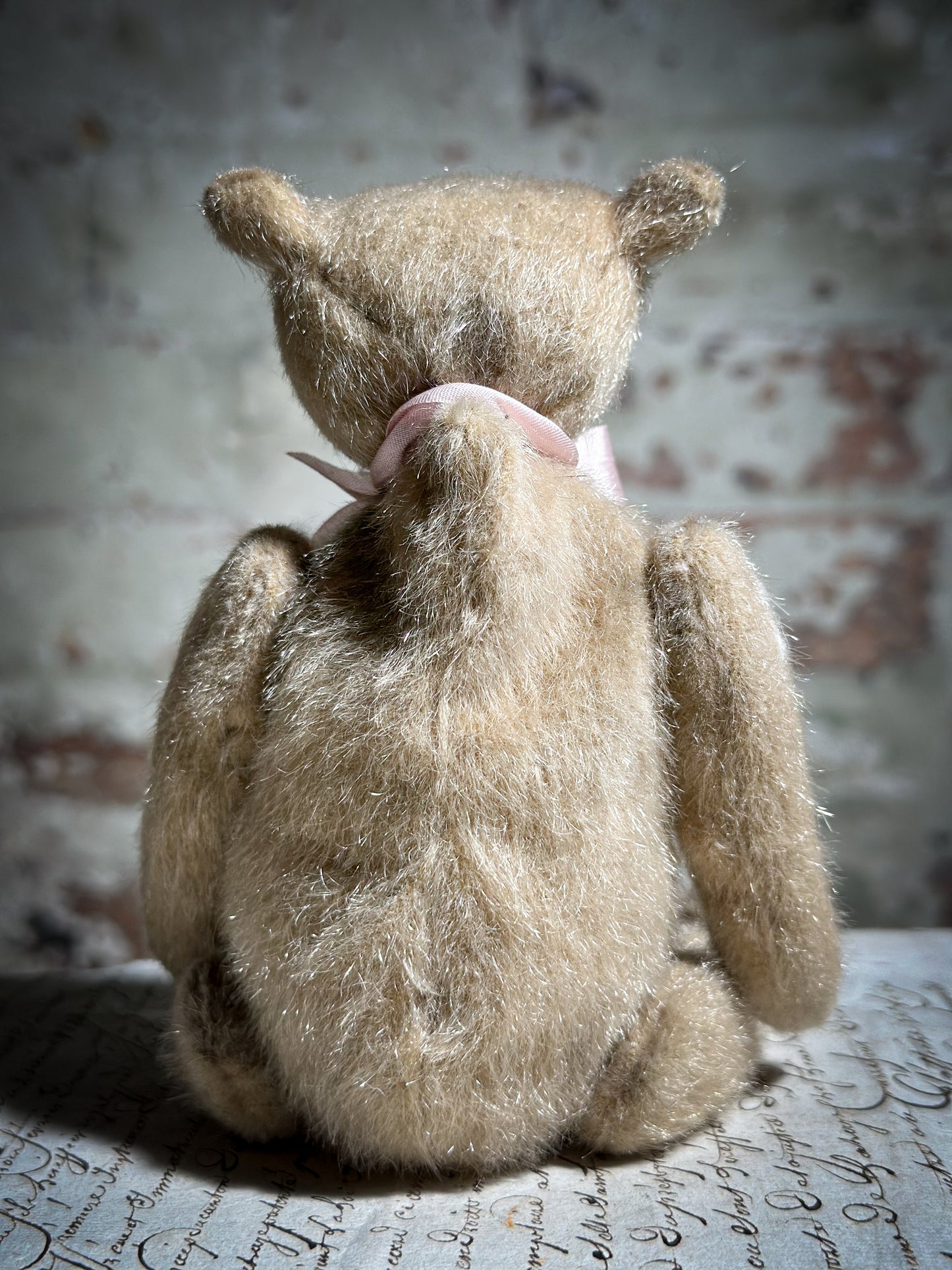 A beautiful hand made tiny jointed collector’s teddy bear with pale pink antique ribbon and bell and heart charm