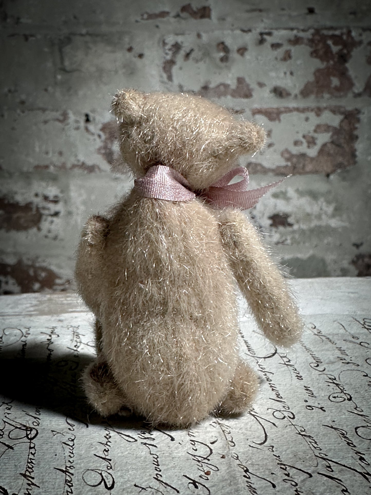 A beautiful hand made tiny jointed collector’s teddy bear with pale pink antique ribbon and bell and heart charm