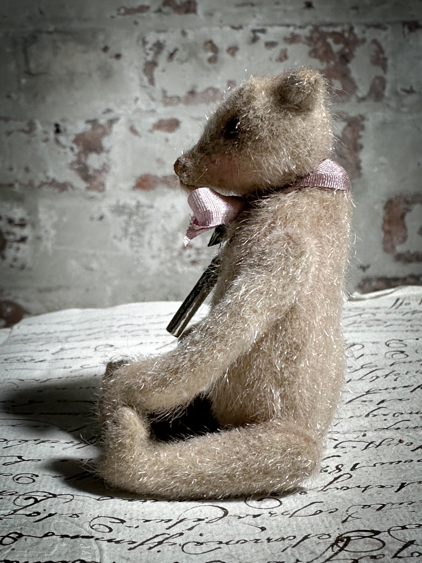 A beautiful hand made tiny jointed collector’s teddy bear with pale pink antique ribbon and bell and heart charm