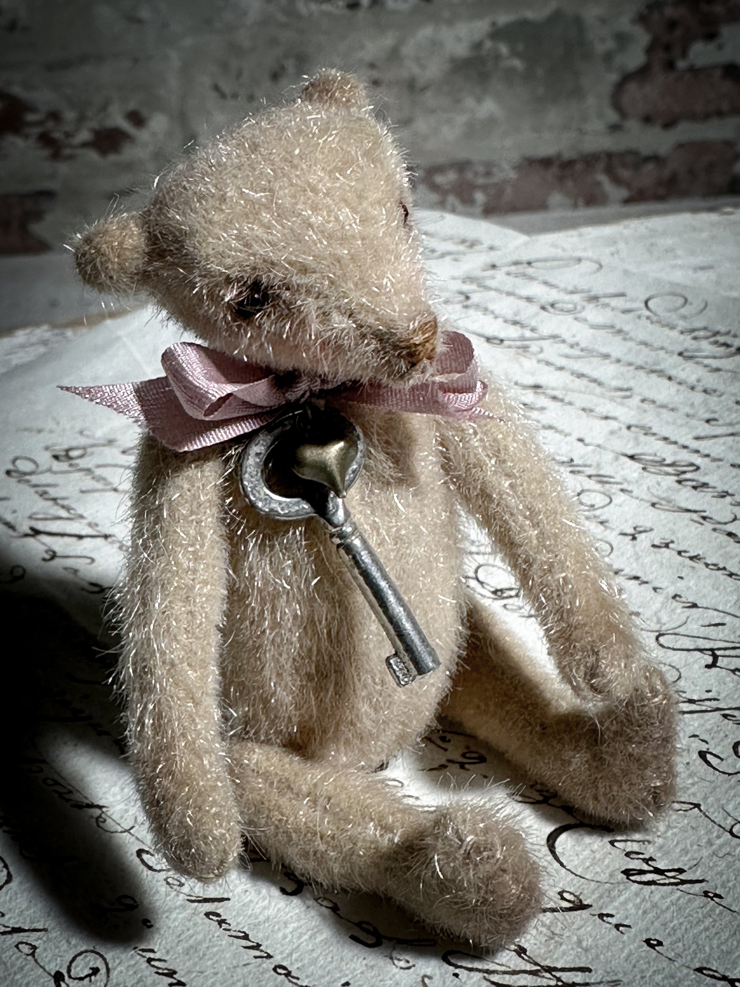 A beautiful hand made tiny jointed collector’s teddy bear with pale pink antique ribbon and bell and heart charm