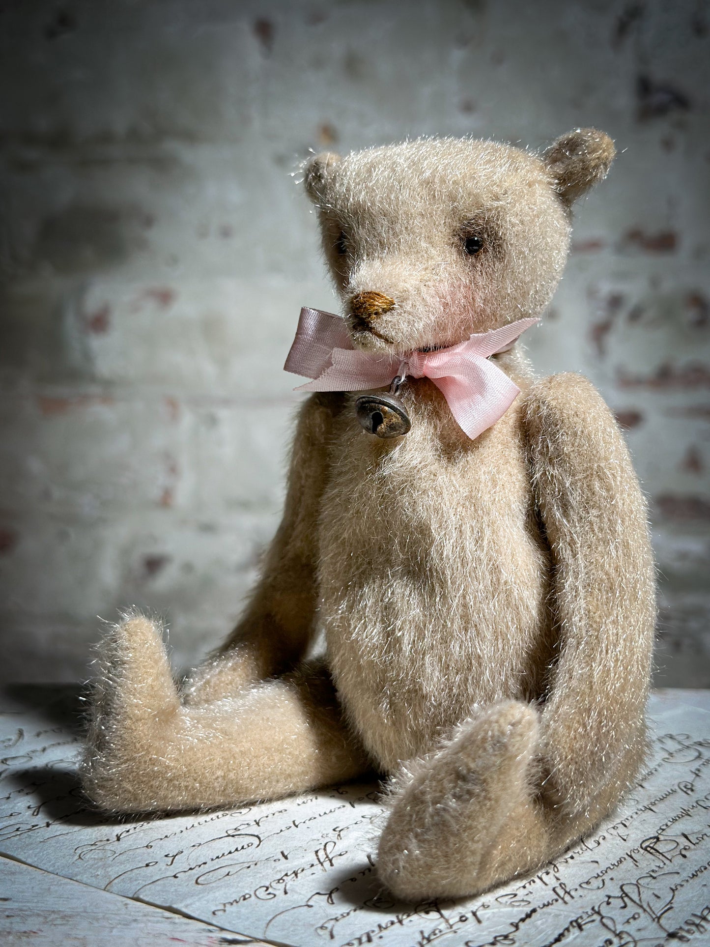 A beautiful hand made tiny jointed collector’s teddy bear with pale pink antique ribbon and bell and heart charm