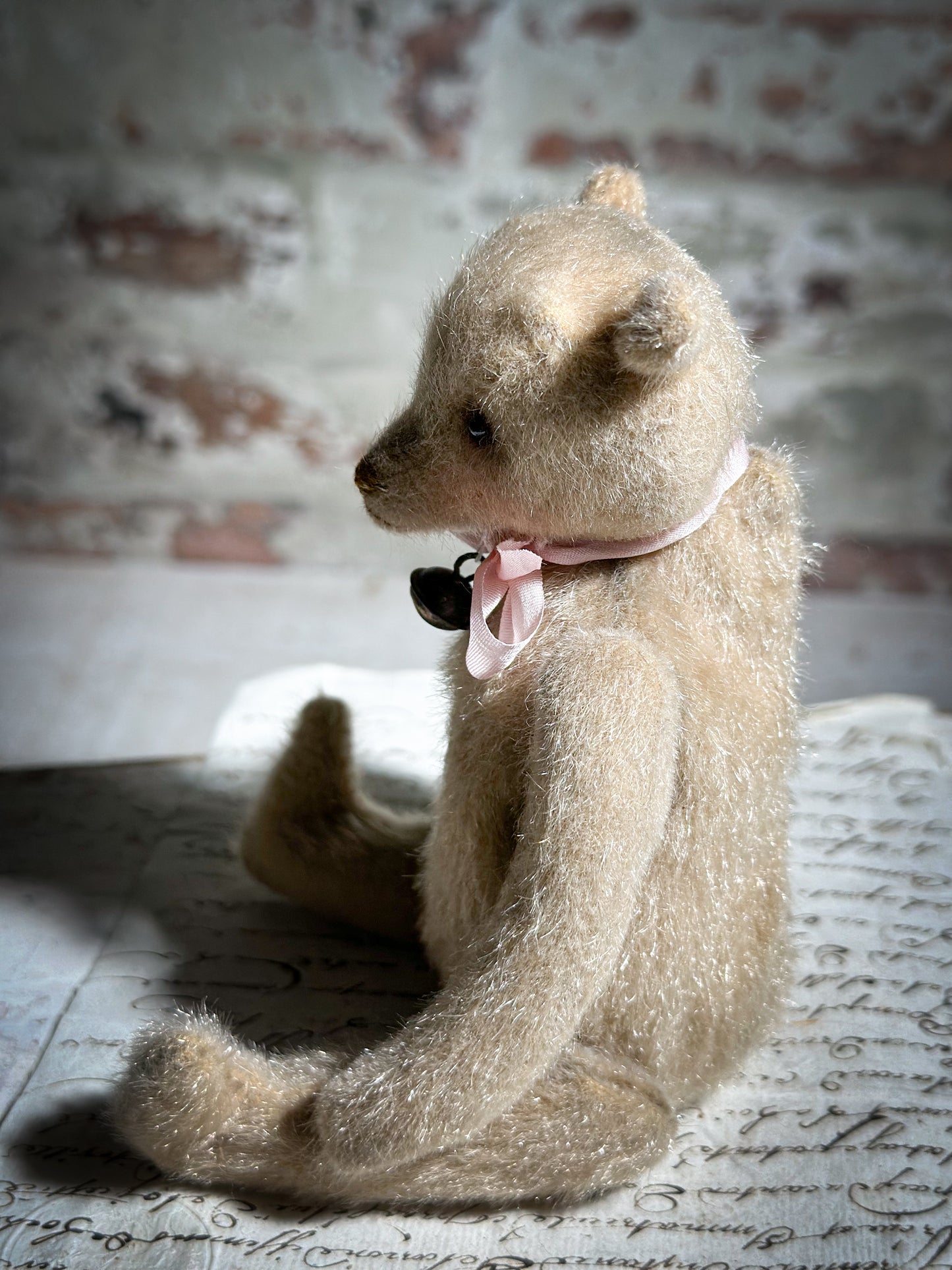 A beautiful hand made tiny jointed collector’s teddy bear with pale pink antique ribbon and bell and heart charm