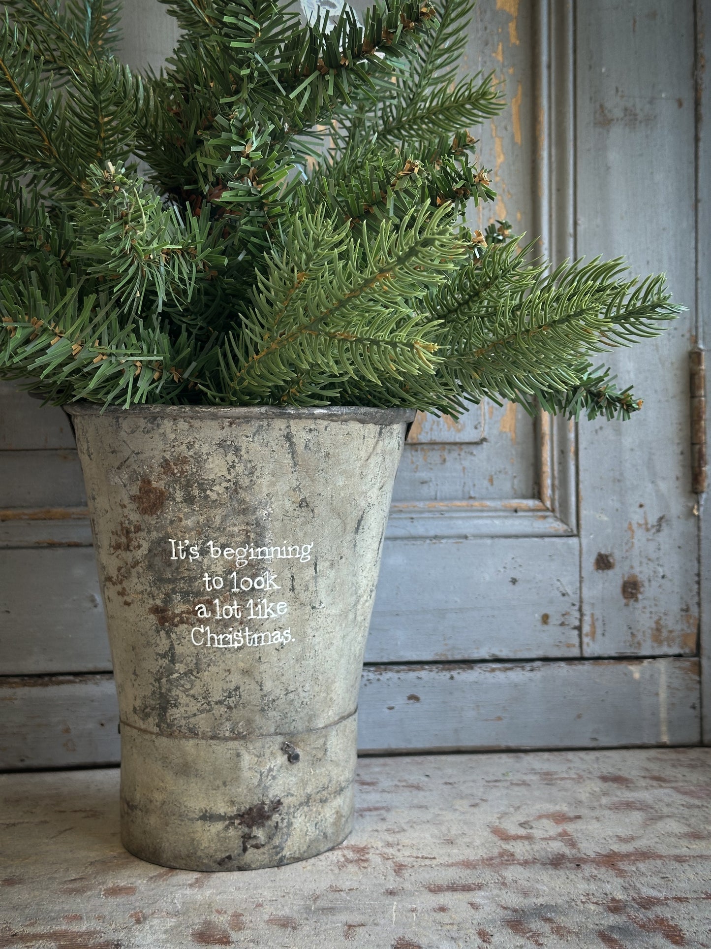 A Recycled Metal Mini Christmas Tree Bucket With A Hand Painted Quote