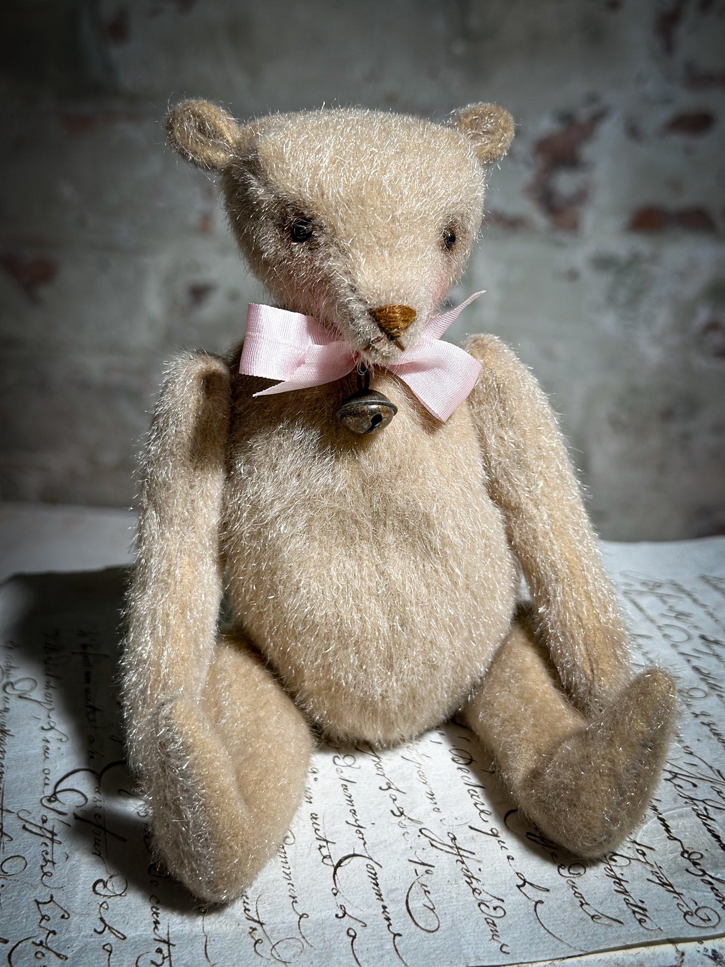 A beautiful hand made tiny jointed collector’s teddy bear with pale pink antique ribbon and bell and heart charm